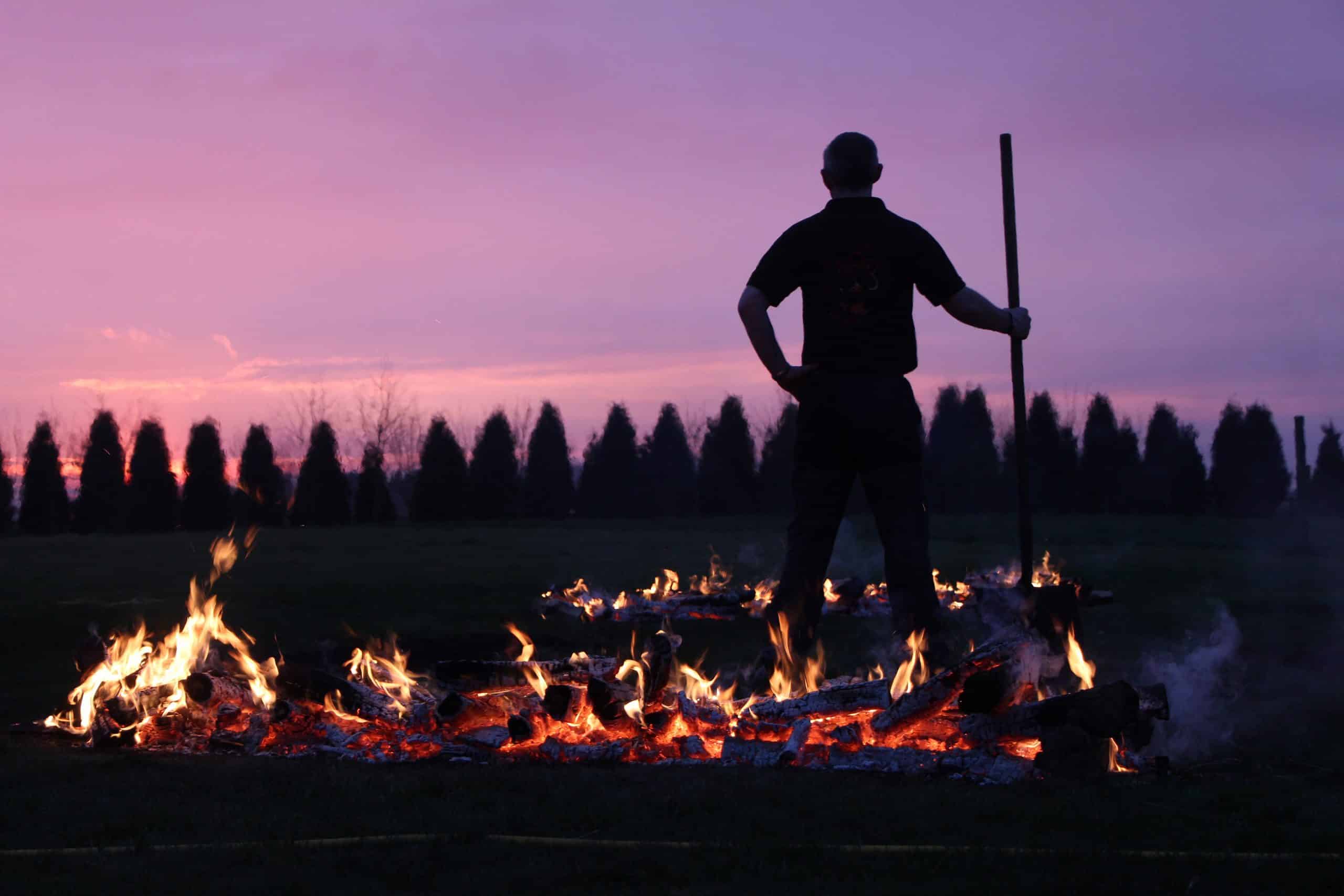 Silhouette against purple sky of man standing between two fires a holding handle of a tool